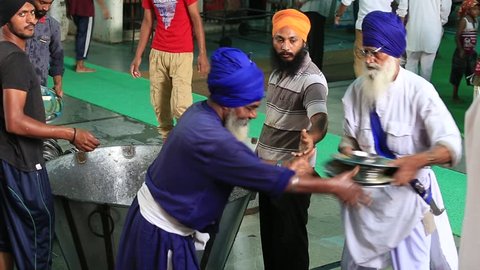 AMRITSAR, INDIA - SEPTEMBER 27, 2014: Unidentified poor indian people clean dishes at a soup kitchen in the Sikh Golden Temple