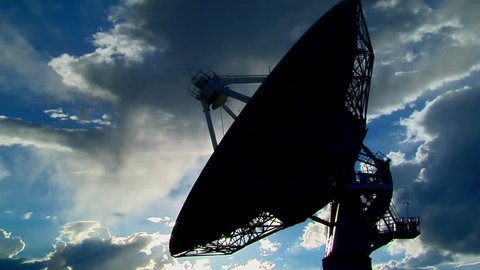 A satellite dish moves in time-lapse and is silhouetted against the sky