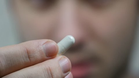 An extreme close up of a man putting a pill in his mouth. Man takes tablet with glass of water