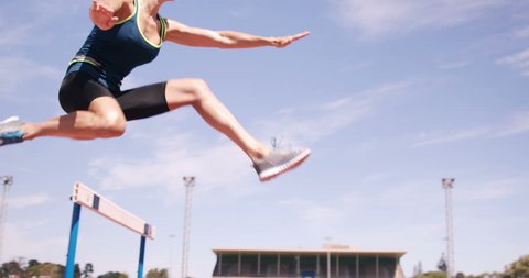 Woman practicing hurdle race on athletic ground