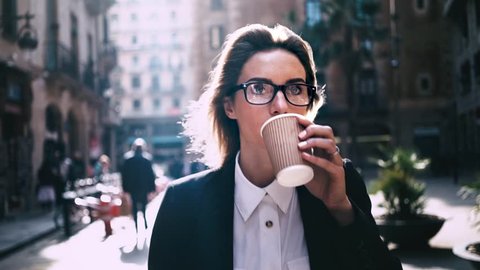 Portrait of young attractive businesswoman drinking coffee to go on a break and using modern smartphone outdoors, sunshine, slow motion