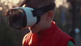 Little boy with surprise and pleasure uses virtual reality helmet and moves around itself outdoor