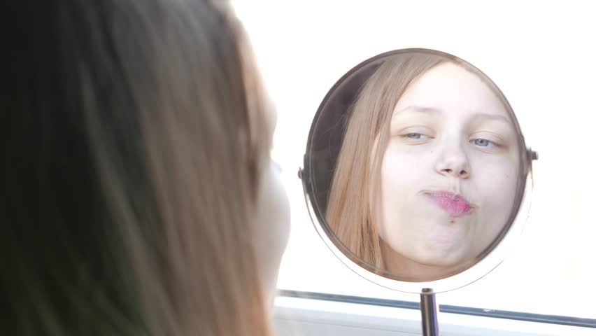 Beauty model teenage girl looking in the mirror and checking her skin, applying make up. 4K