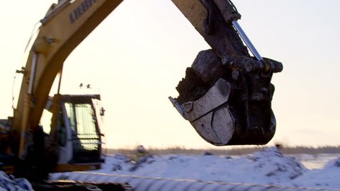 Excavator digging the ground in winter sunset