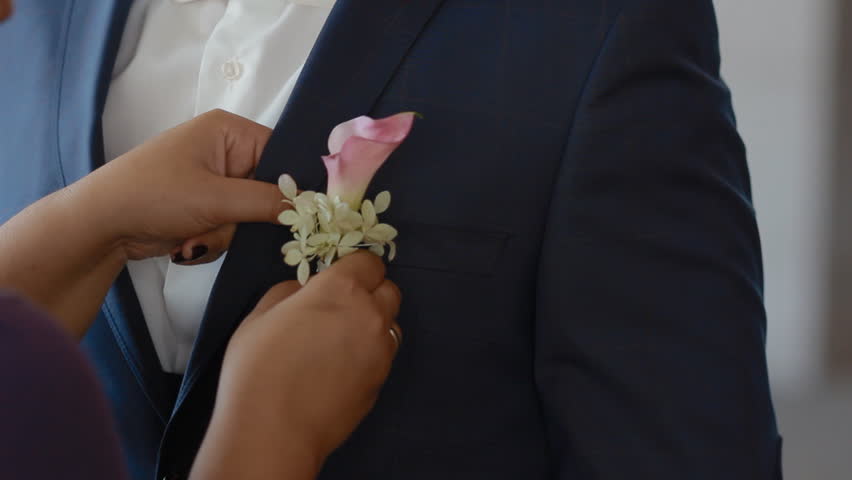 Portrait of young caucasian man. Groom in blue suit with white bowtie. Woman correct the boutonniere on his suit.