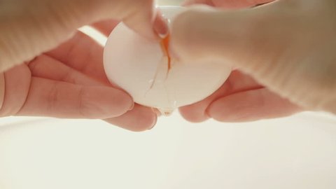 Female hands holding cracked egg over a white bowl
