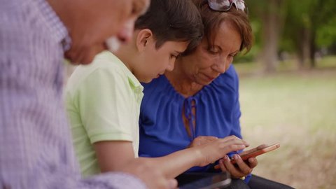 Old and young people together, seniors and children in family relationship, generations with child and elderly persons. Boy teaching happy grandparents how to use smartphone for internet and email
