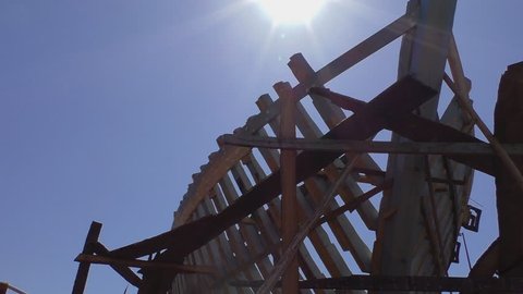 Wooden ship construction or building in the shipyard.Tilt down against blue sky and strong sunlight shows skeleton or framework of new big boats or fishing trawlers being built 