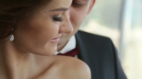 Groom gently touches beautiful face of his bride close up. Very tender moment