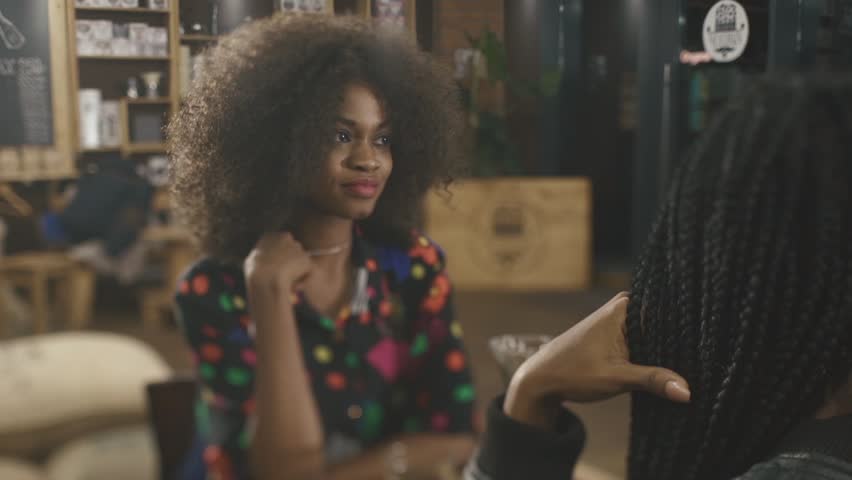 Two pretty elegant african females having coffee and talking in the cafe
