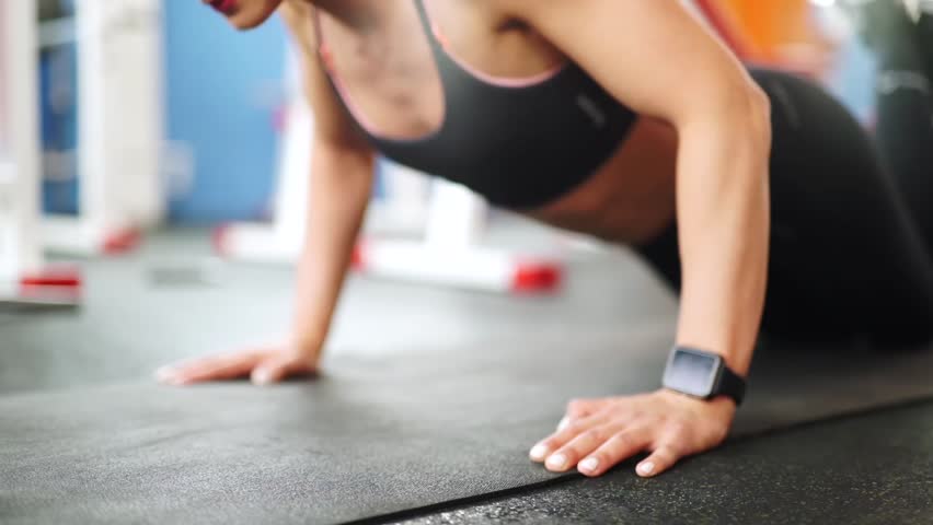 Athletic young woman doing push-ups. Close-up front view of smart watch
