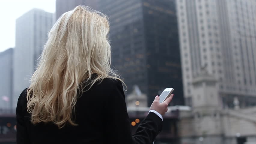 Attractive Blonde Business Woman Using Smartphone Commuter in City, Pretty Young Business Woman Talking by Phone Against Complex of Modern Office Buildings.a Beautiful Girl With a Black Bag in Hand,a
