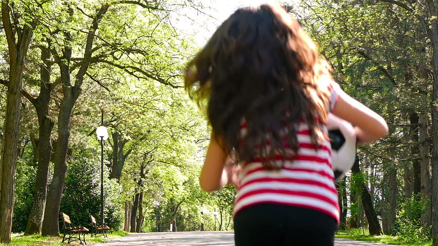 Young girl with soccer ball running in a park