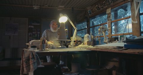 Old artist modeling a clay sculpture in his small studio
