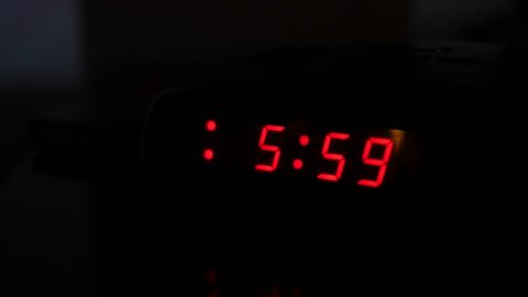 A man turns off the alarm when a digital alarm clock turns to six o'clock and turns on a light