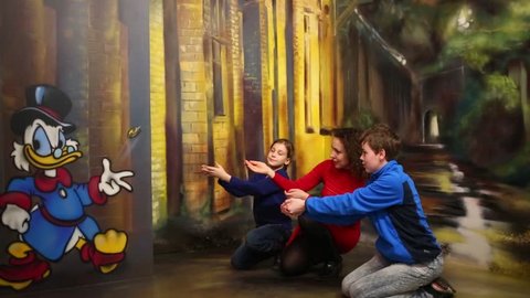 MOSCOW - MAR 24, 2015: Woman, girl and boy (with model releases) catch coin of Scrooge McDuck in optical illusions Museum at VDNKh