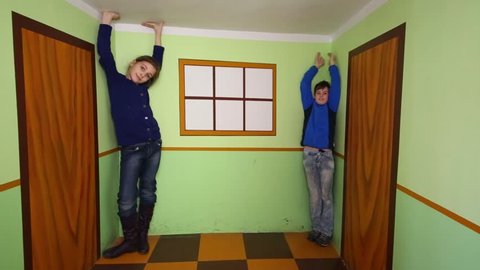 Happy boy and girl pose in room with optical illusion