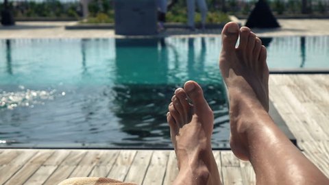 Male feet on daybed by swimming pool, super slow motion 240fps
