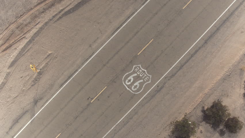 AERIAL: Black SUV car driving along historic Route 66 through the vast desert. People traveling, road trip on empty countryside road through America on sunny summer vacation