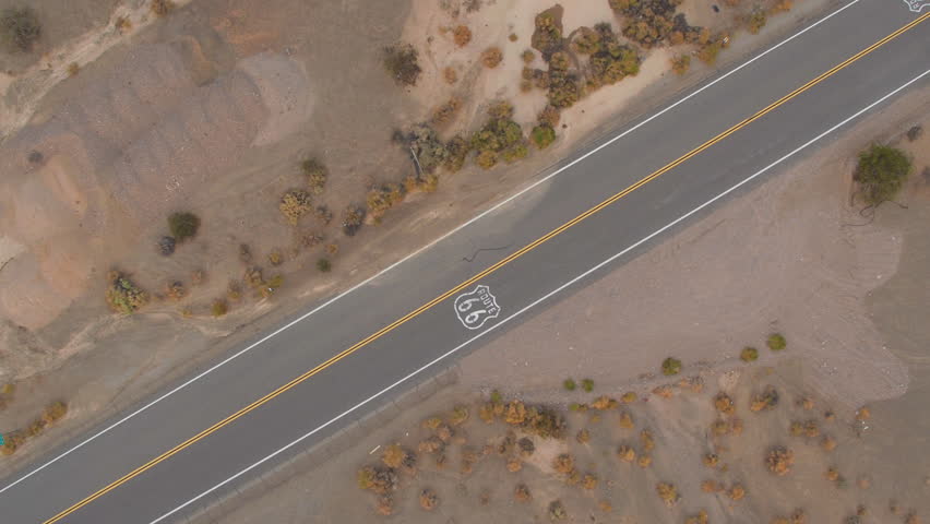AERIAL: Cars driving along historic Route 66 through the vast desert. People traveling, road trip on empty countryside road through America on sunny summer vacation