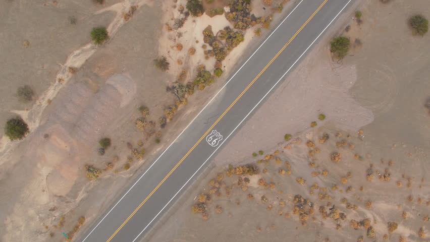 AERIAL: Black SUV car driving along historic Route 66 through the vast desert. People traveling, road trip on empty countryside road through America on sunny summer vacation