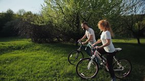 Series of 5 video: Couple riding bicycles on the green meadow at sunset.