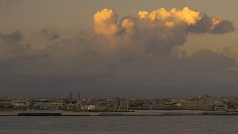 The golden light of sunset lights up clouds along the Naples, Italy industrial shoreline in POV clip form passing cruise ship at dusk.