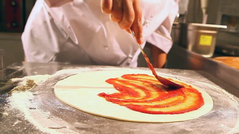 Chef rolls dough for pizza. then he smears red sauce. fast motion