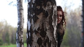 Pretty happy woman looks out of birch in autumn forest