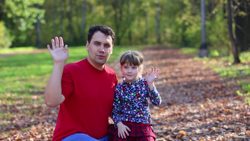 Little girl and her father wave hands and play in sunny autumn park
