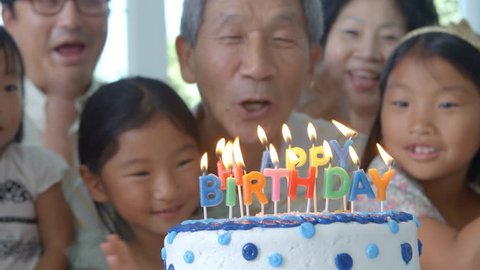 Grandfather Blows Out Candles On Birthday Cake