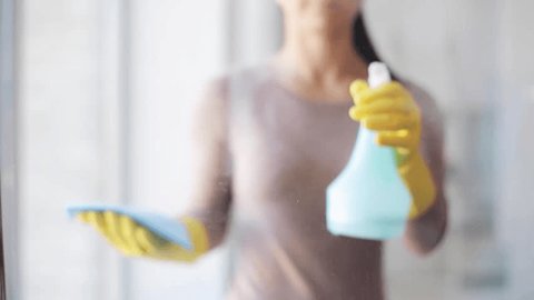 people, housework and housekeeping concept - woman in gloves cleaning window with rag and cleanser spray at home