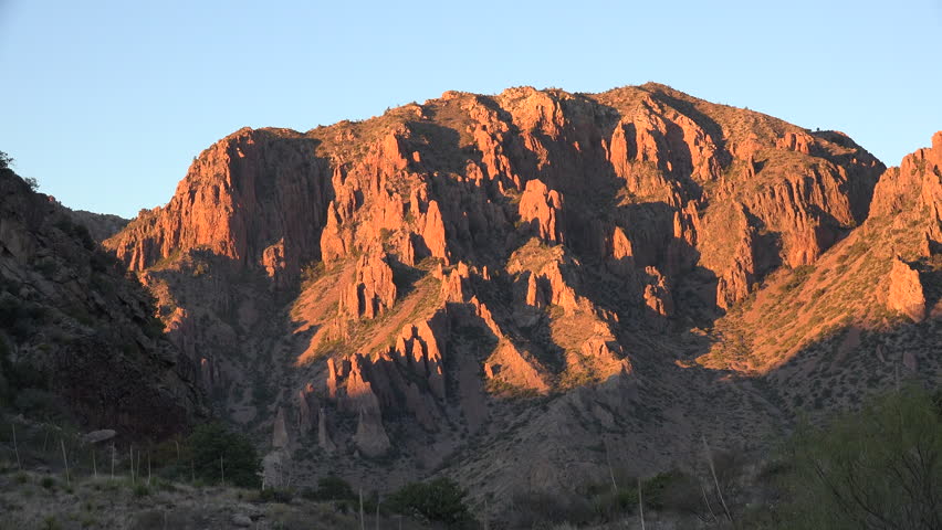 A large jagged rock stands out against a light orange sky after sunset in The Window in the Chisos Mountains of Big Bend National Park.