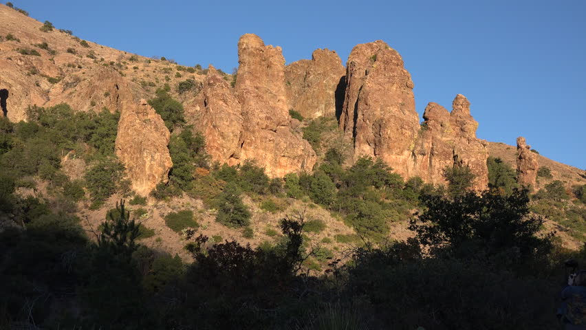 Tall rock formations on a hill against a blue sky in afternoon light in the Chisos Mountains of Big Bend National Park.
