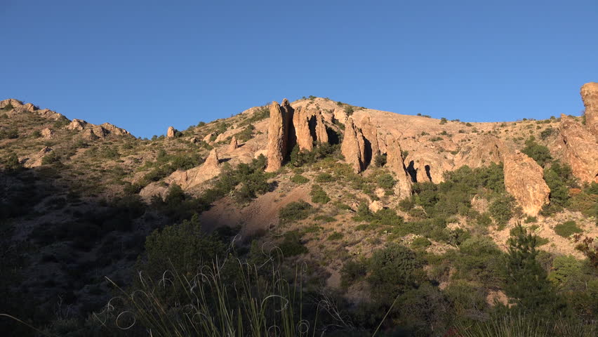 Tall, starkly lit rock formations in evening light against a blue sky in the Chisos Mountains of Big Bend National Park.