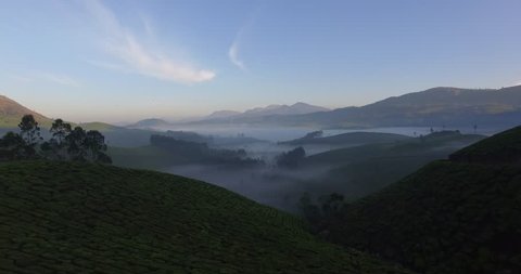 Aerial shot, moving down over green hills into morning fog in Munnar, India