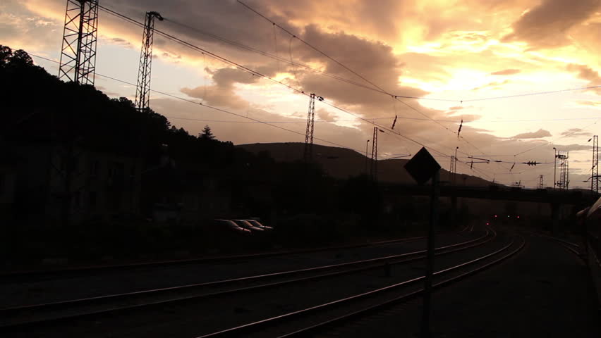 Train passing under a bridge near station at sunset