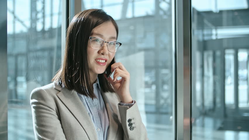 Young Asian businesswoman standing in the moving elevator and talking on the cell phone