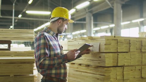 Worker counts wood stock using a tablet computer at a lumber factory warehouse. Shot on RED Cinema Camera in 4K (UHD).