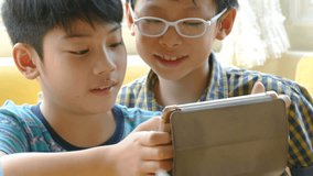 Young asian boy playing games on a touchscreen tablet with a friend