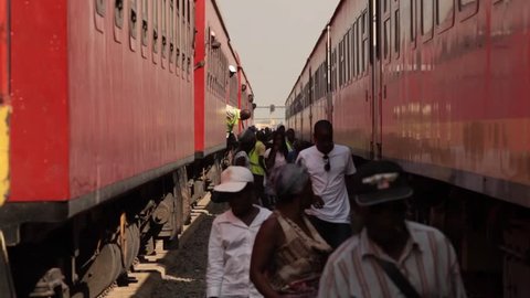 Luanda, Angola - circa 2011 - Medium shot between two stationary red coloured trains. Passengers descend from the trains and walk between the carriages towards the camera.