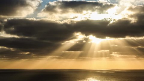timelapse of clouds crossing the amazing sky over the sea or ocean at sunset. Sun rays emerge through the clouds. The clouds cross slowly from right to left and appear to be orange blue and purple. 