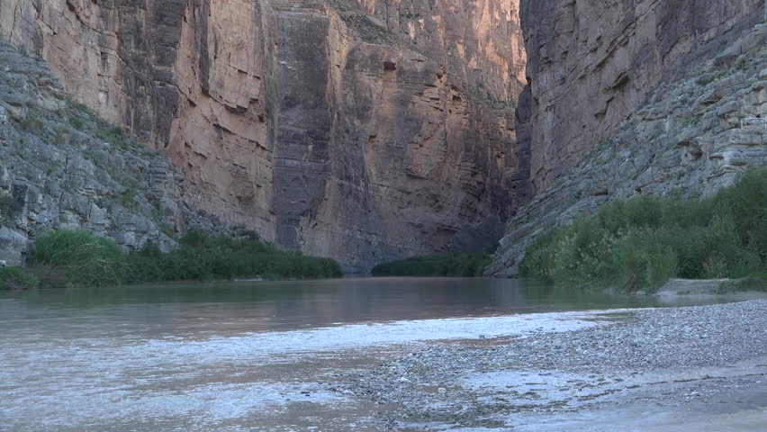 Sun shines on an ocotillo that frames a view of the mouth of Santa Elena Canyon in Big Bend National Park zooms out.