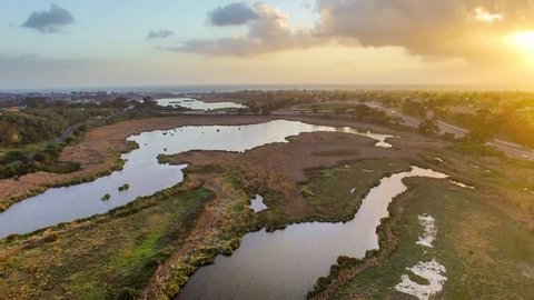 Aerial footage of warm sunset over Buena Vista Lagoon with views of the Southern California coastal cities of Oceanside and Carlsbad, I-5 freeway and Pacific Ocean in distance