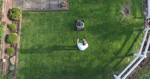 An aerial view of a man mowing the lawn.  	