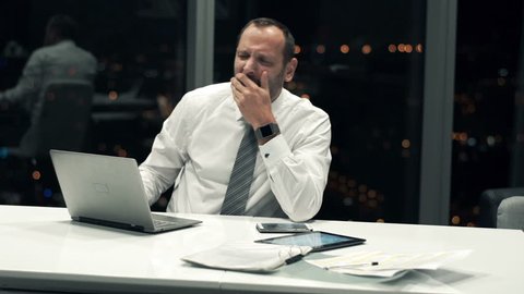 Tired businessman with laptop yawning in the office during night
