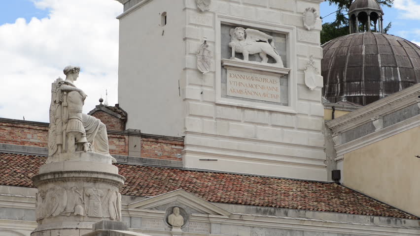 The great clock in Piazza Liberta in Udine. One of many tourism attraction points in Piazza della Liberta in Udine, Italy. A tower with a clock with roman numbers and sun in the middle.