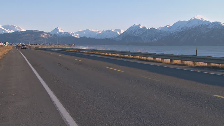 Late afternoon traffic on the Homer Spit Road in Alaska, Kenai Mountains beyond.