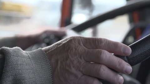 Steering wheel in use. Close up slow motion shot of hands of a senior man driving the vehicle.