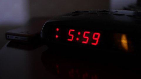 A digital alarm clock turns on at six o'clock and a man turns it off